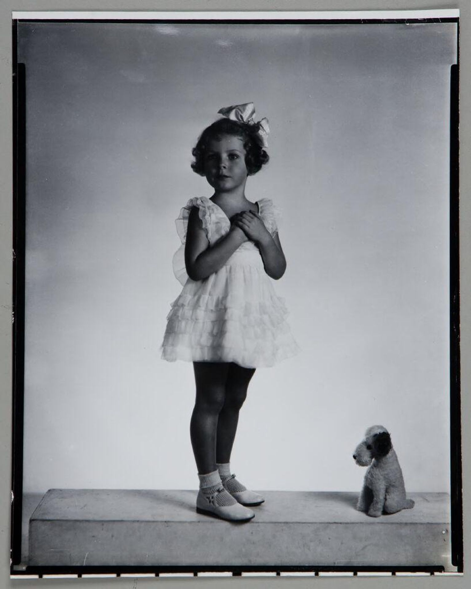 Untitled (girl in ruffled dress with hands clasped at chest, stuffed dog to her side) by Paul Gittings