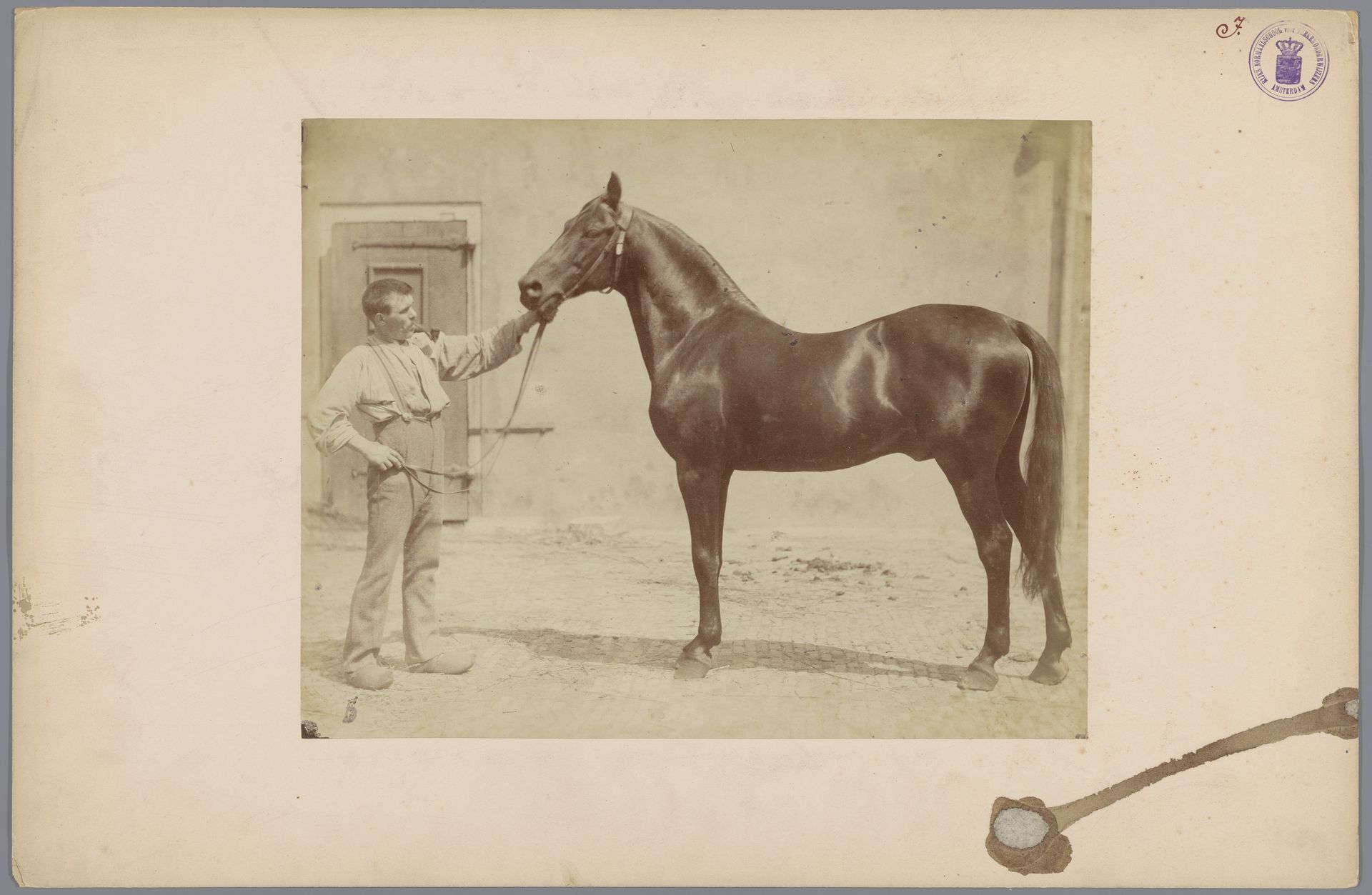 Man met een pijp en klompen met een donker paard op een binnenplaats by Willem Frederik Vinkenbos