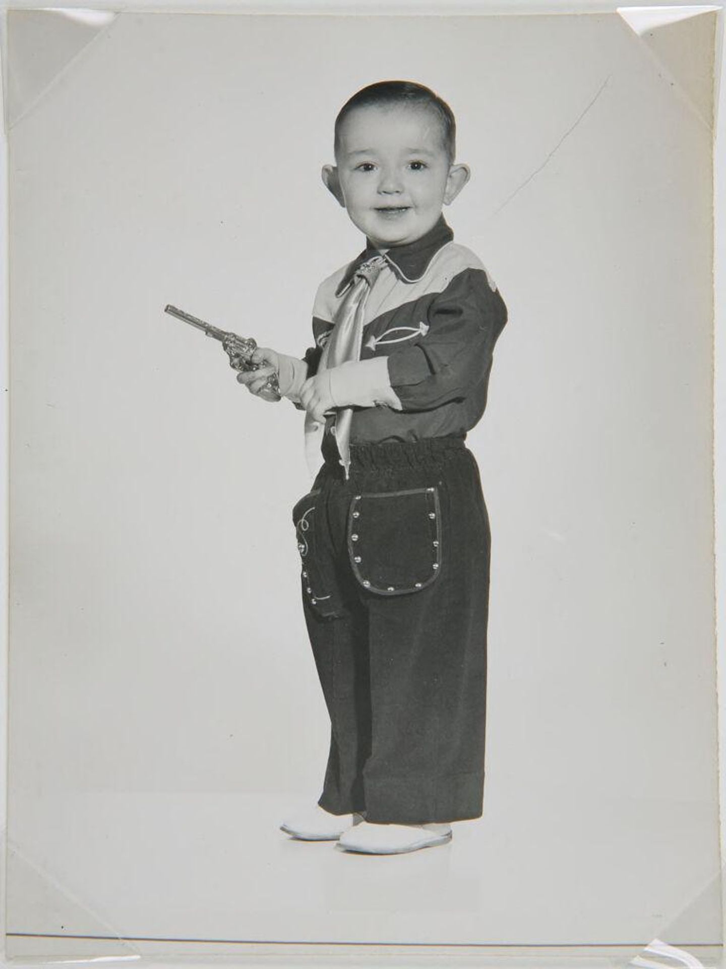 Untitled (little boy in cowboy outfit, holding gun, looking at camera) by John Deusing