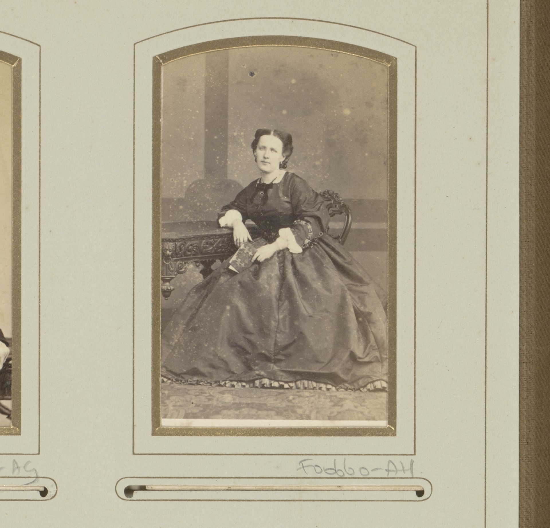 Portret van een vrouw, zittend aan een tafel met fotoalbum in de hand by Maes & Michaux