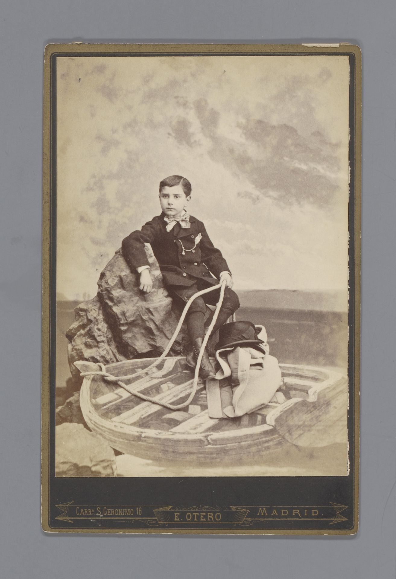 Studioportret van een onbekende jongen op een rots boven een roeiboot by E. Otero