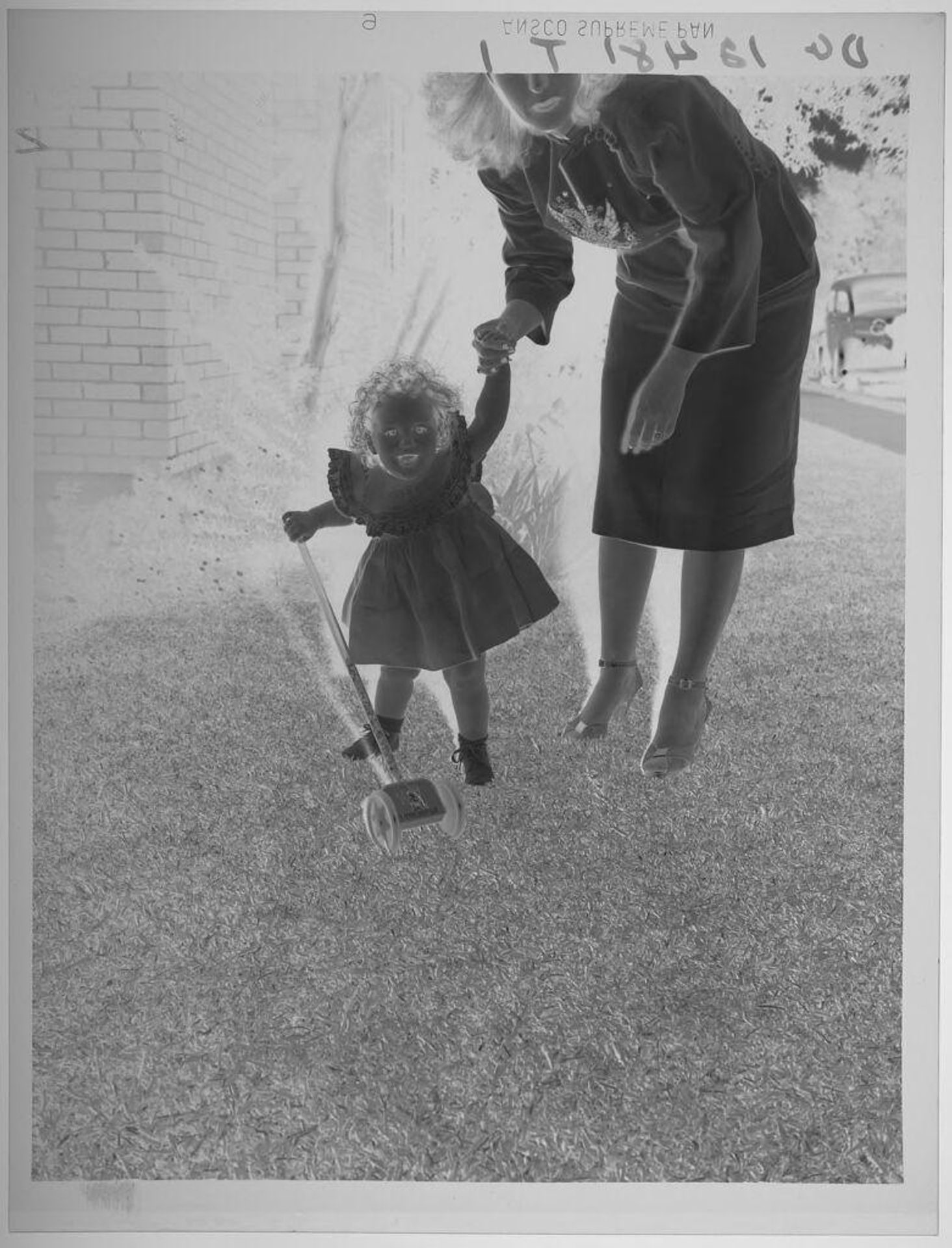 Untitled (little girl pushing toy in grass and holding mother's hand) by Paul Gittings