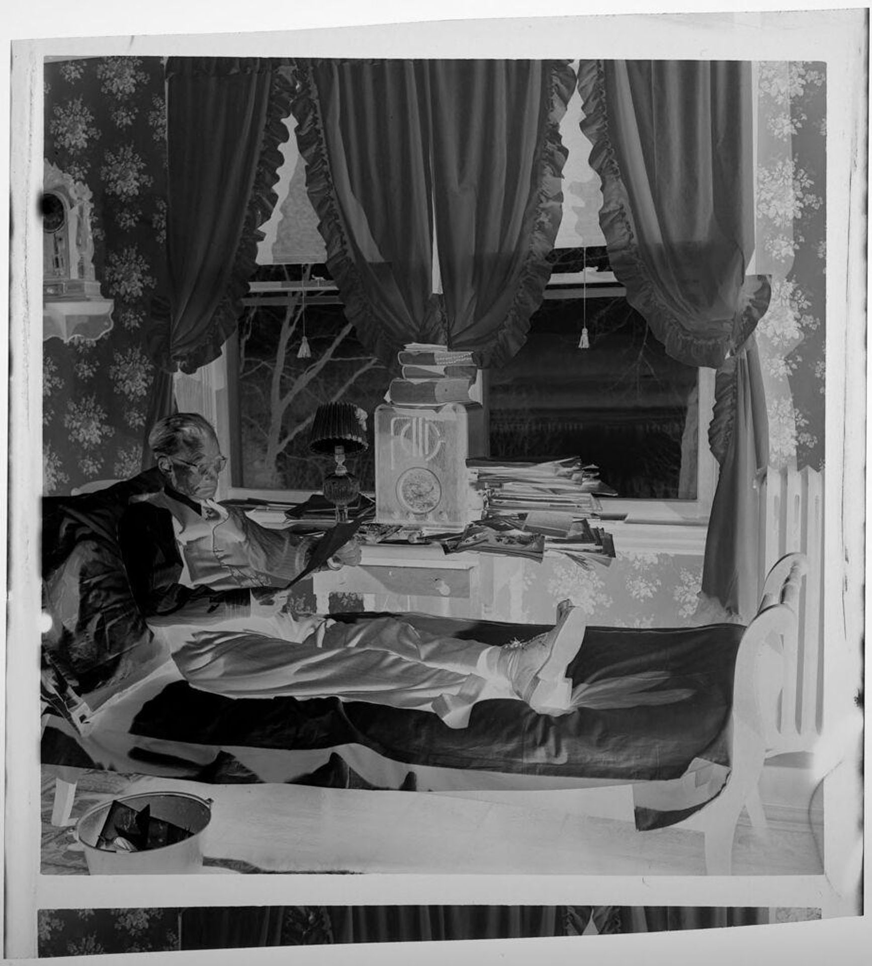 Untitled (elderly man reading papers on day bed, curtains behind) by Jack Gould