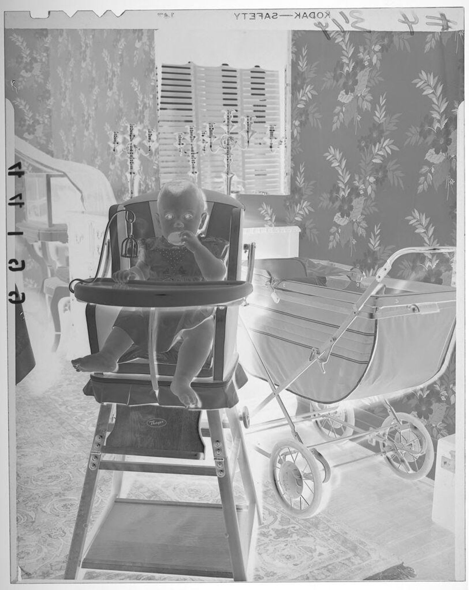 Untitled (baby wearing dress posed sitting in high chair next to stroller) by Martin Schweig