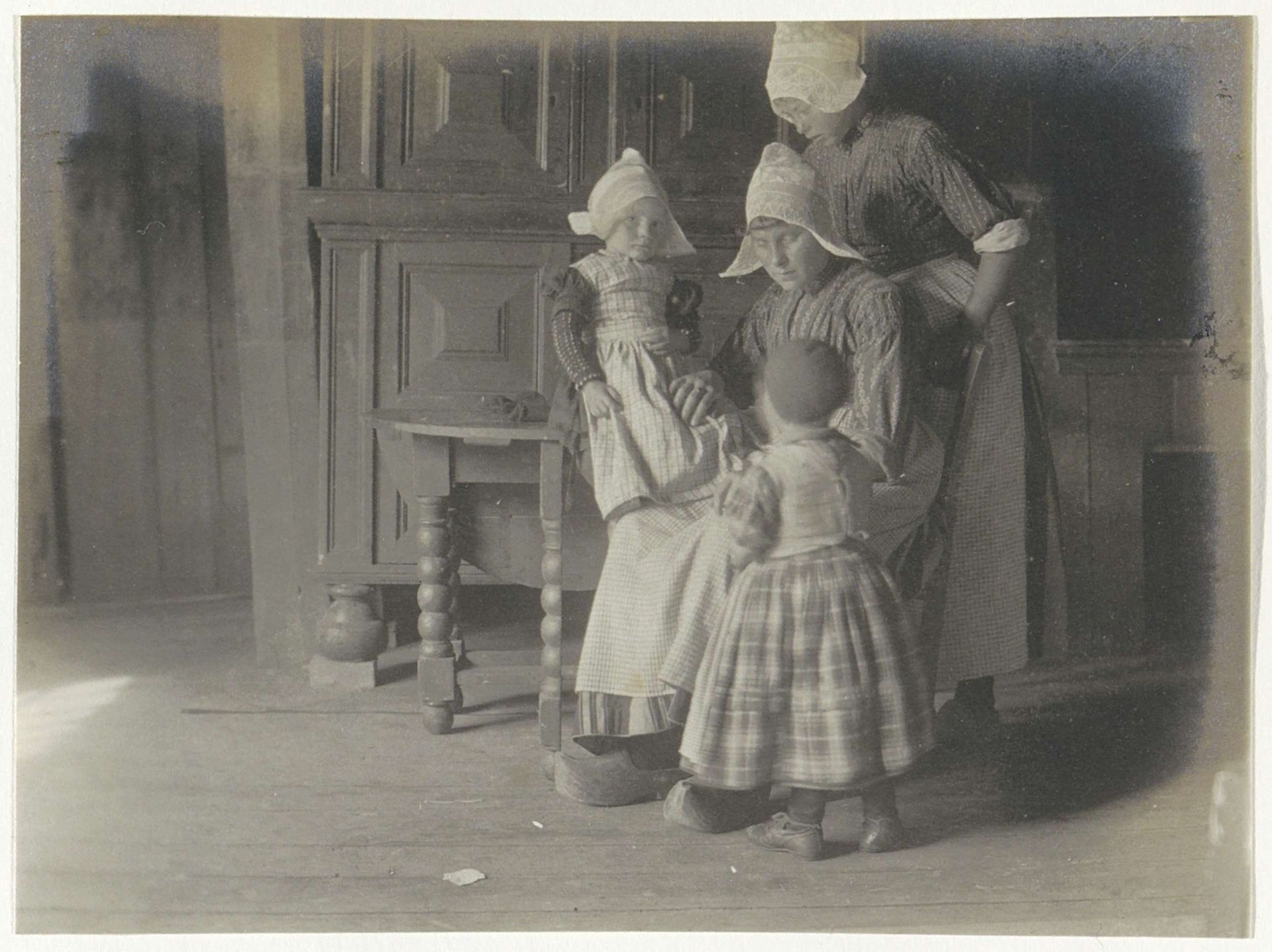 Vrouw met kinderen in klederdracht in een huiskamer, vermoedelijk in Volendam by G. Hidderley