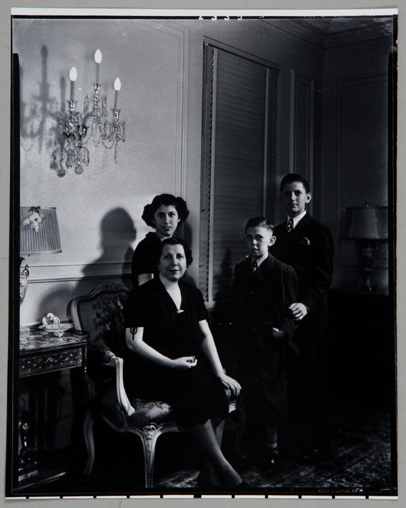 Untitled (mother seated in chair with three children beside her, in living room under chandelier sconce) by Paul Gittings