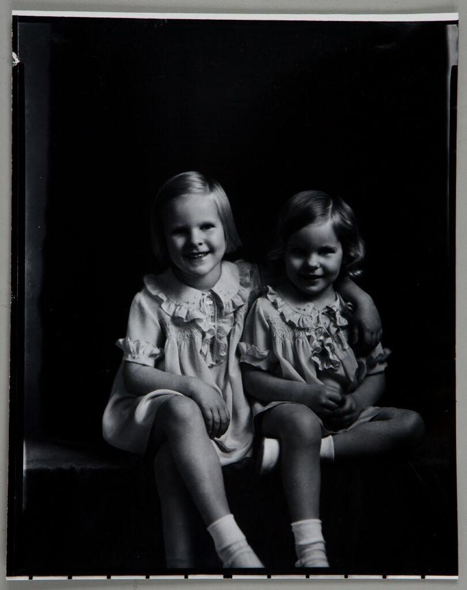 Untitled (two little girls in matching dresses with crossed legs, one with arm around the other) by Paul Gittings