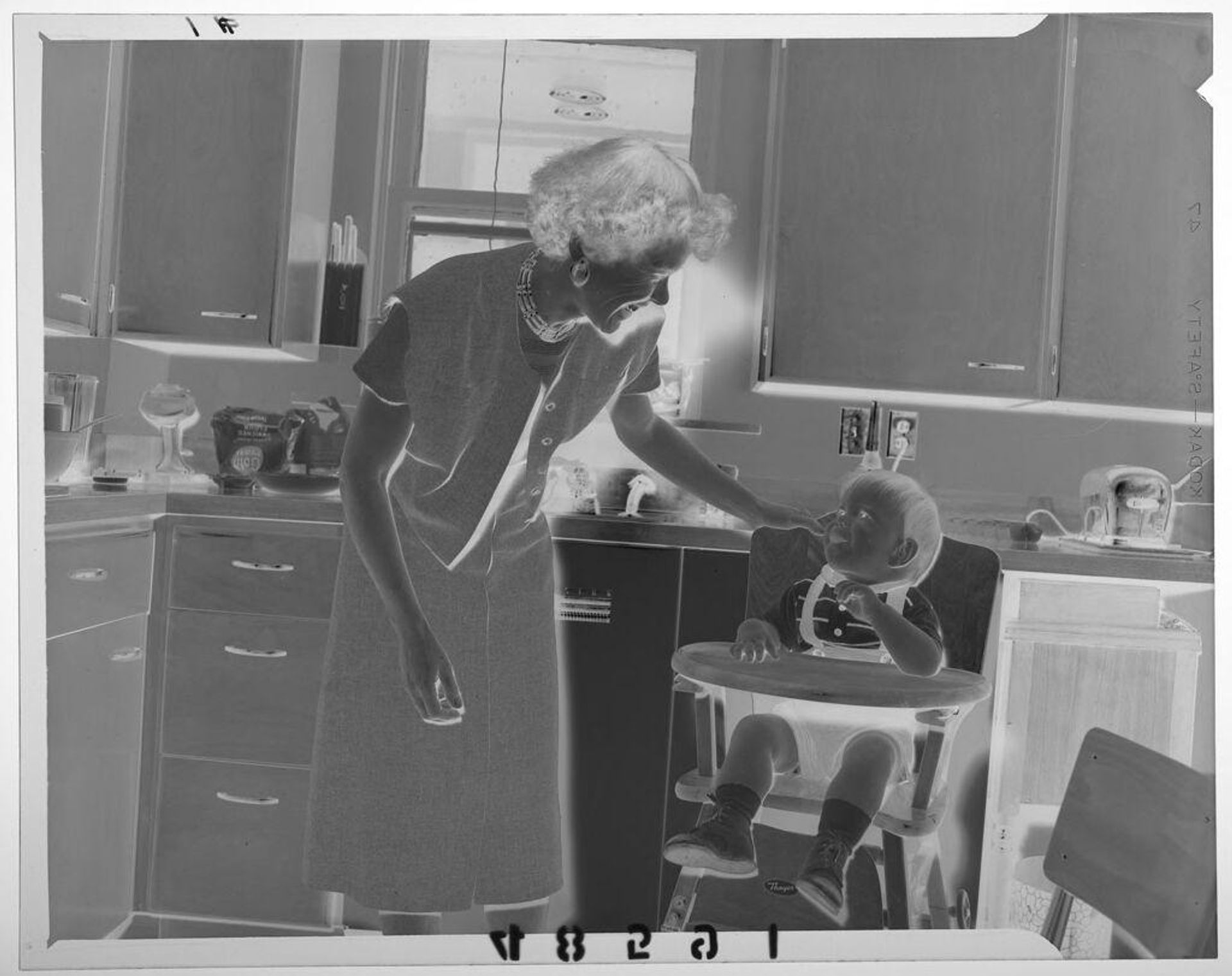 Untitled (mother smiling at baby boy sitting in high chair in kitchen) by Martin Schweig