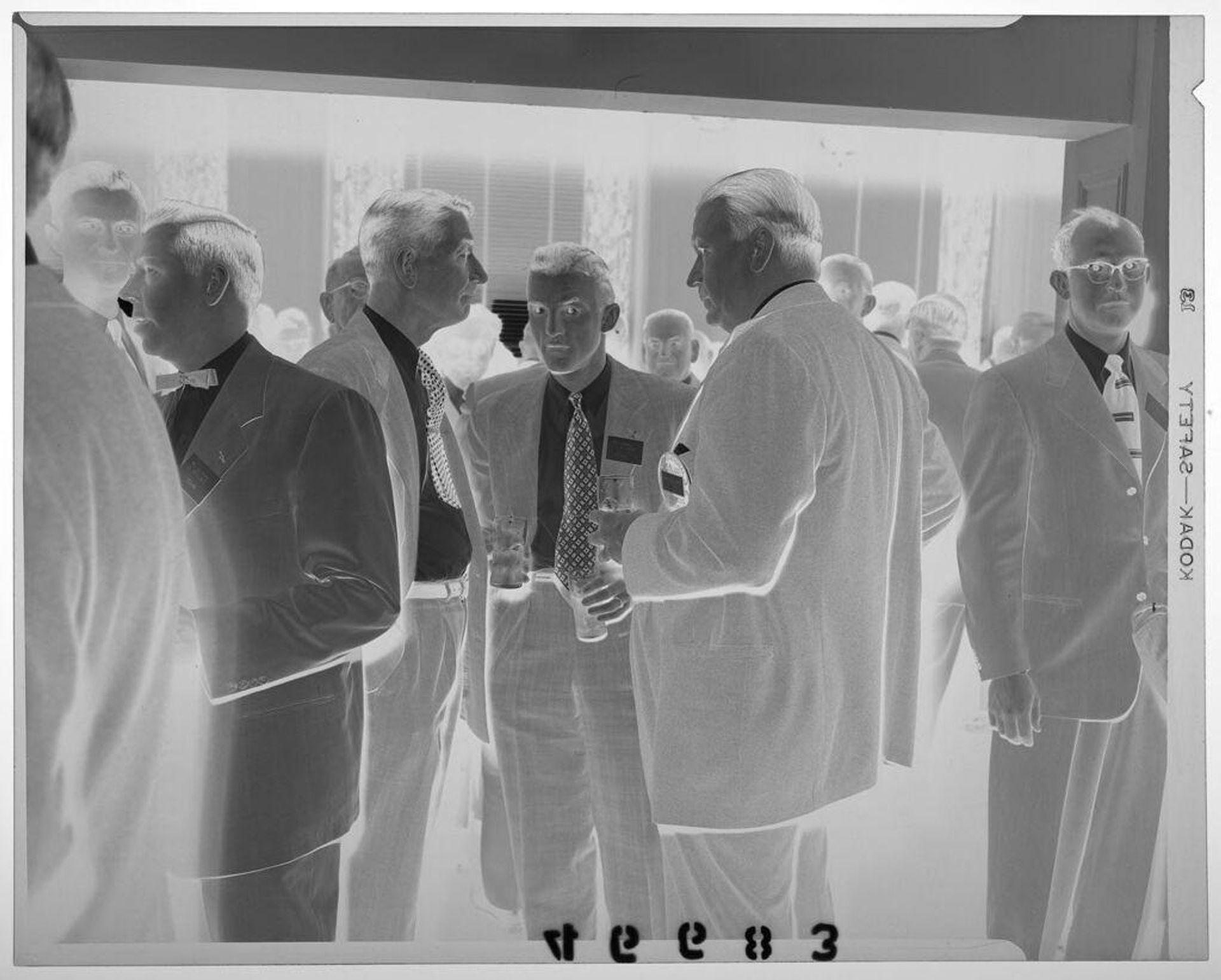 Untitled (three men chatting in conference room surrounded by other men) by Martin Schweig
