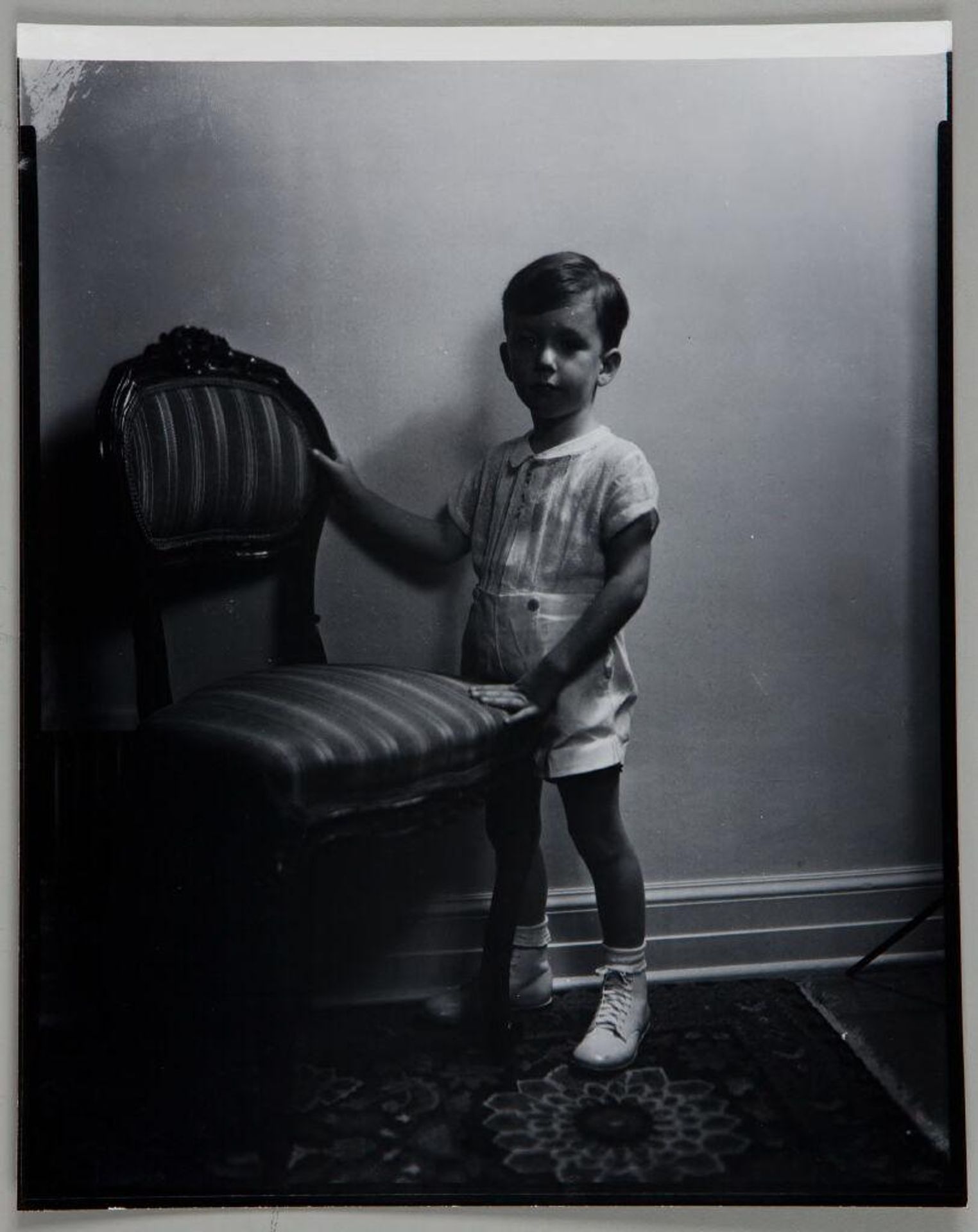 Untitled (young boy in shorts standing with hands on chair) by Paul Gittings