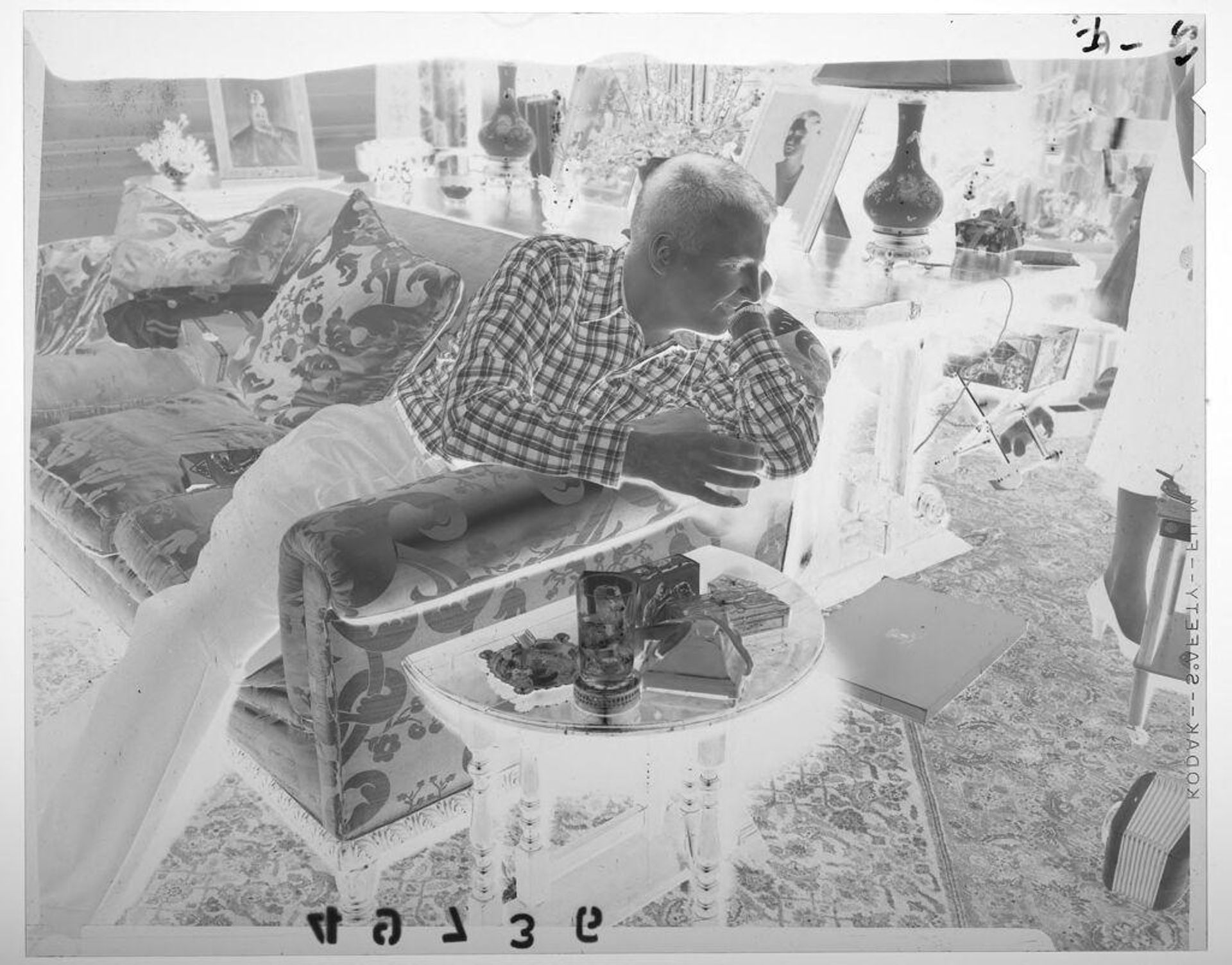 Untitled (man smiling at woman off camera while sitting with drink on couch) by Martin Schweig