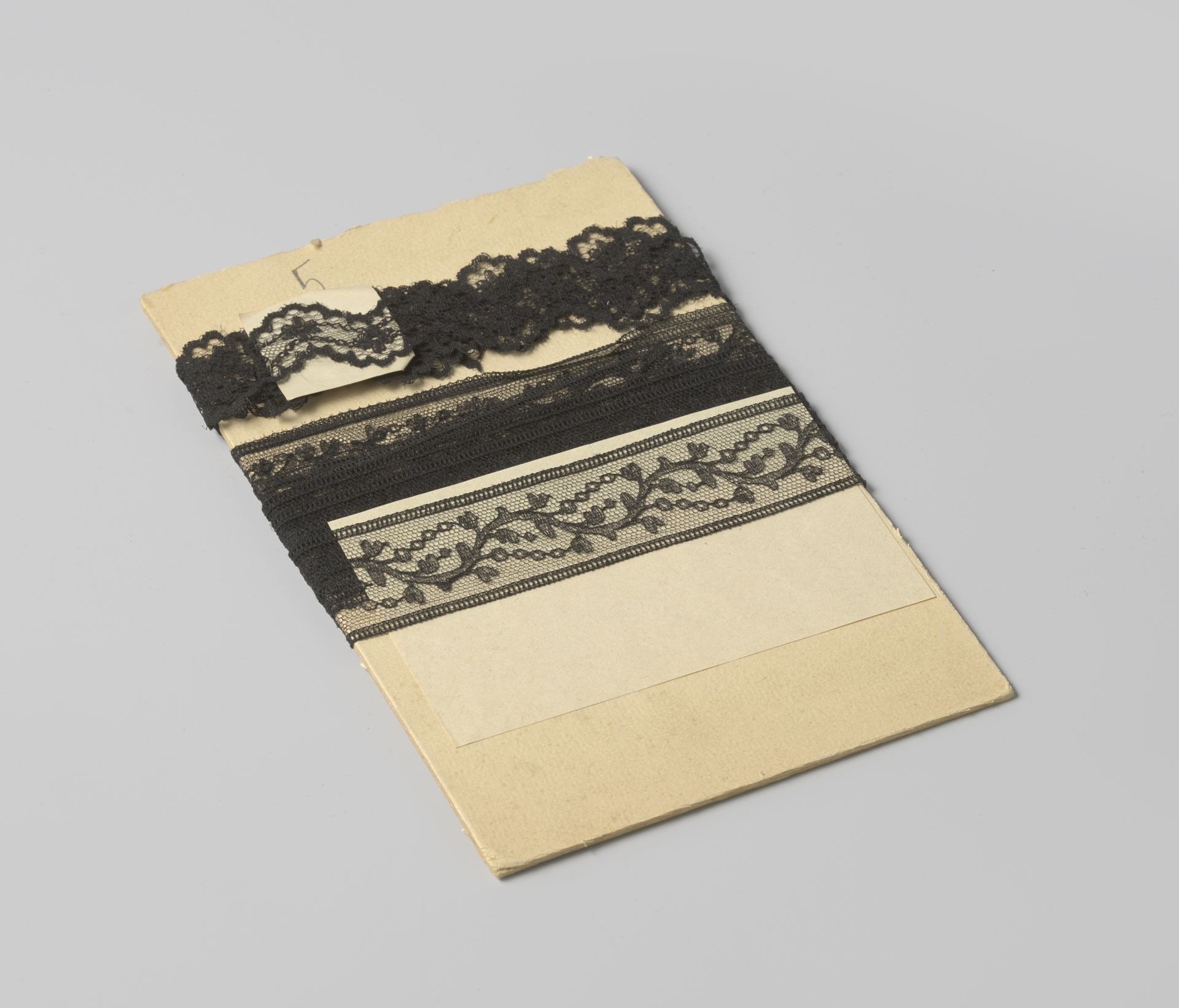 Tussenzetsel van zwarte machinale kant met doorlopend slingerend bladmotief, op karton by Gustav Schnitzler
