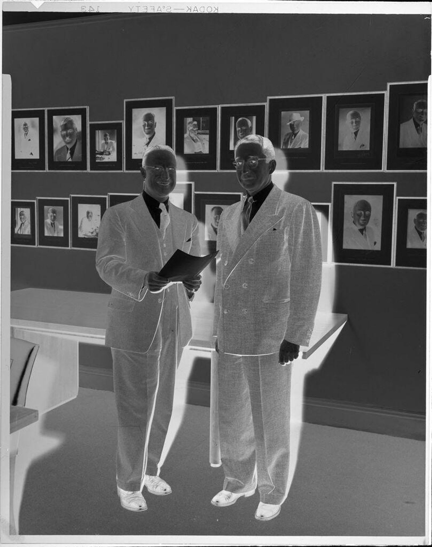Untitled (two men in front of pictures on wall) by Peter James Studio