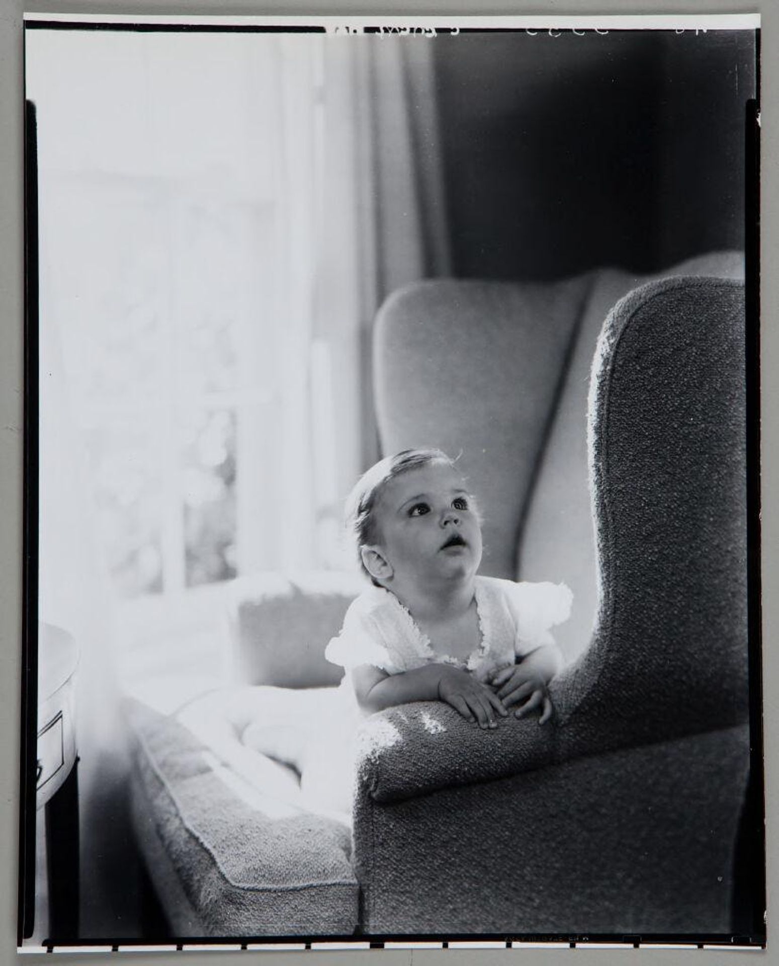 Untitled (toddler in armchair, leaning against arm of chair and looking up) by Paul Gittings