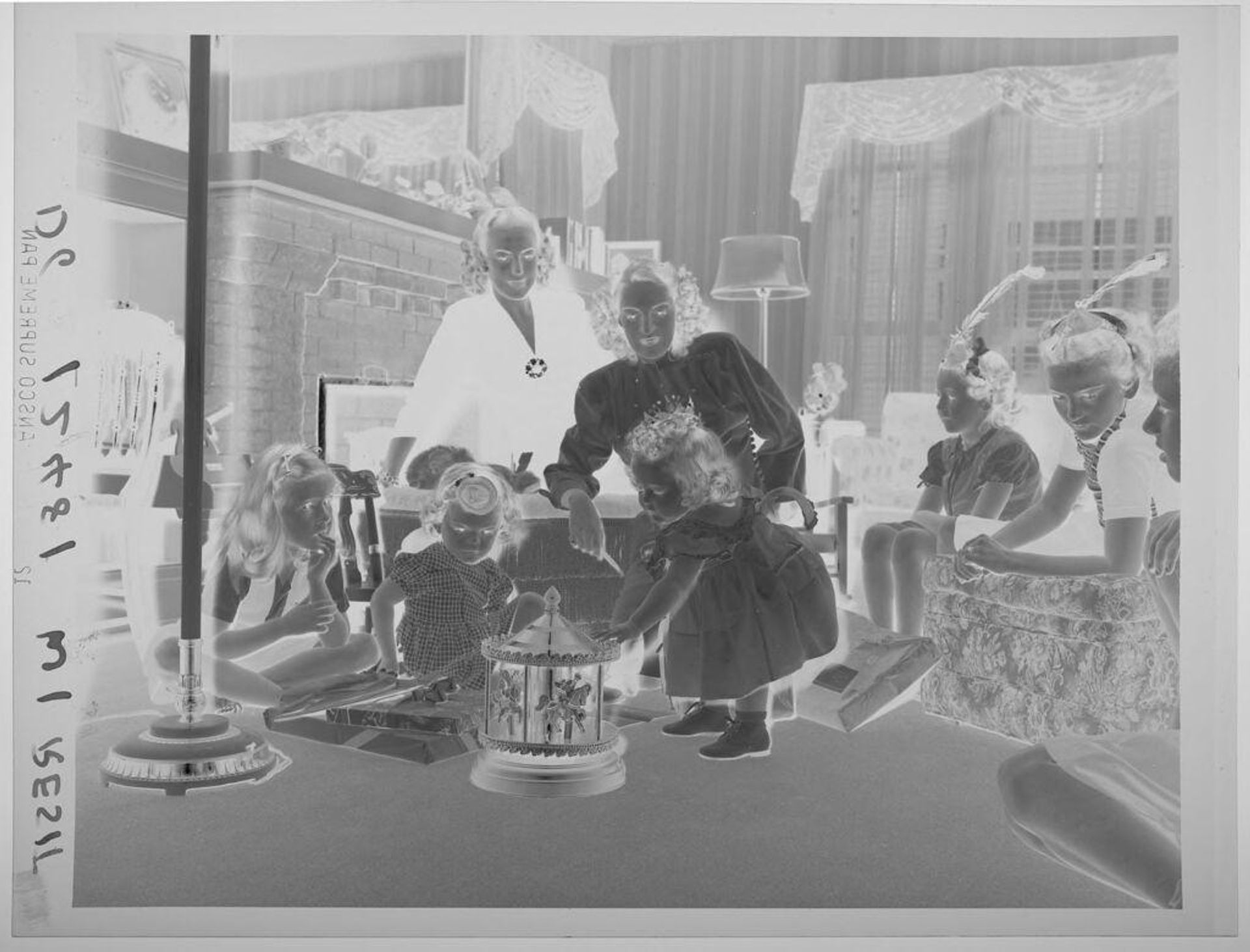 Untitled (little girl touching new toy carousel, others gathered in room for birthday party) by Paul Gittings