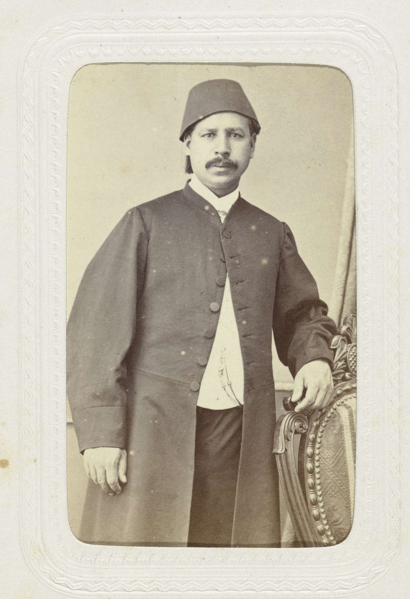 Studioportret van een man met snor in lange jas met op zijn hoofd een fez. by Abdullah Frères