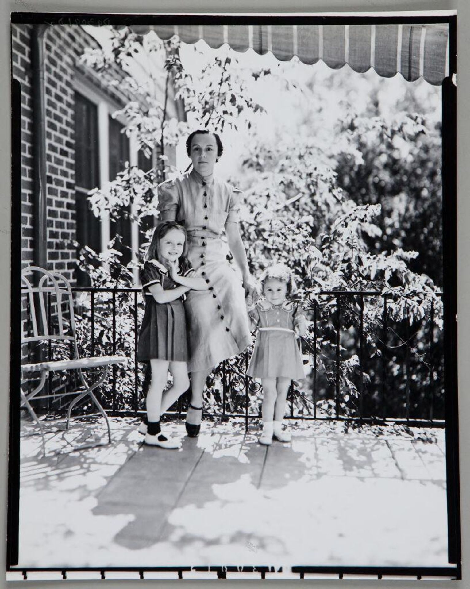 Untitled (woman with two young daughters standing in front of iron railing on porch) by Paul Gittings
