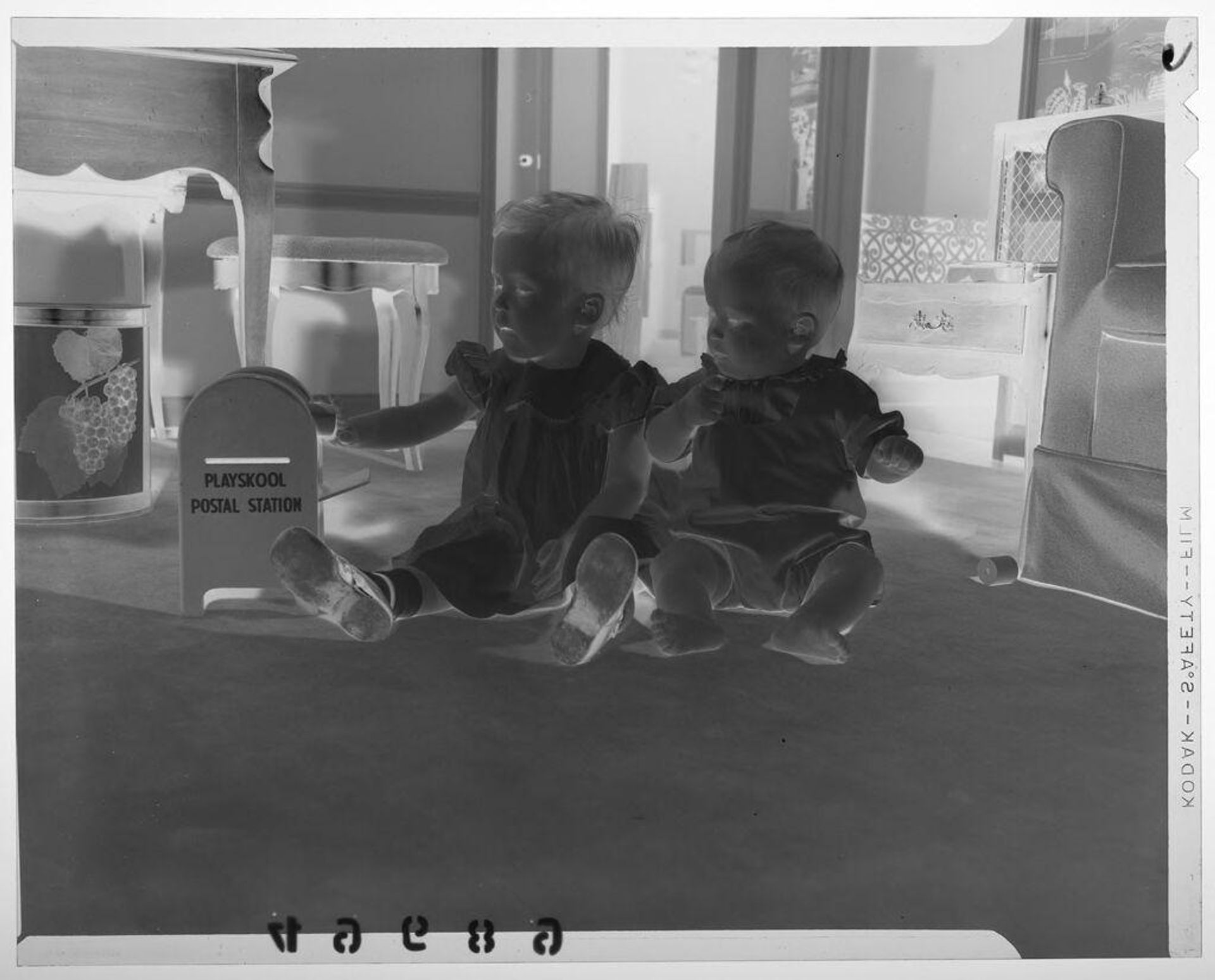 Untitled (very young girl and baby boy posed sitting on floor looking at toy mailbox) by Martin Schweig