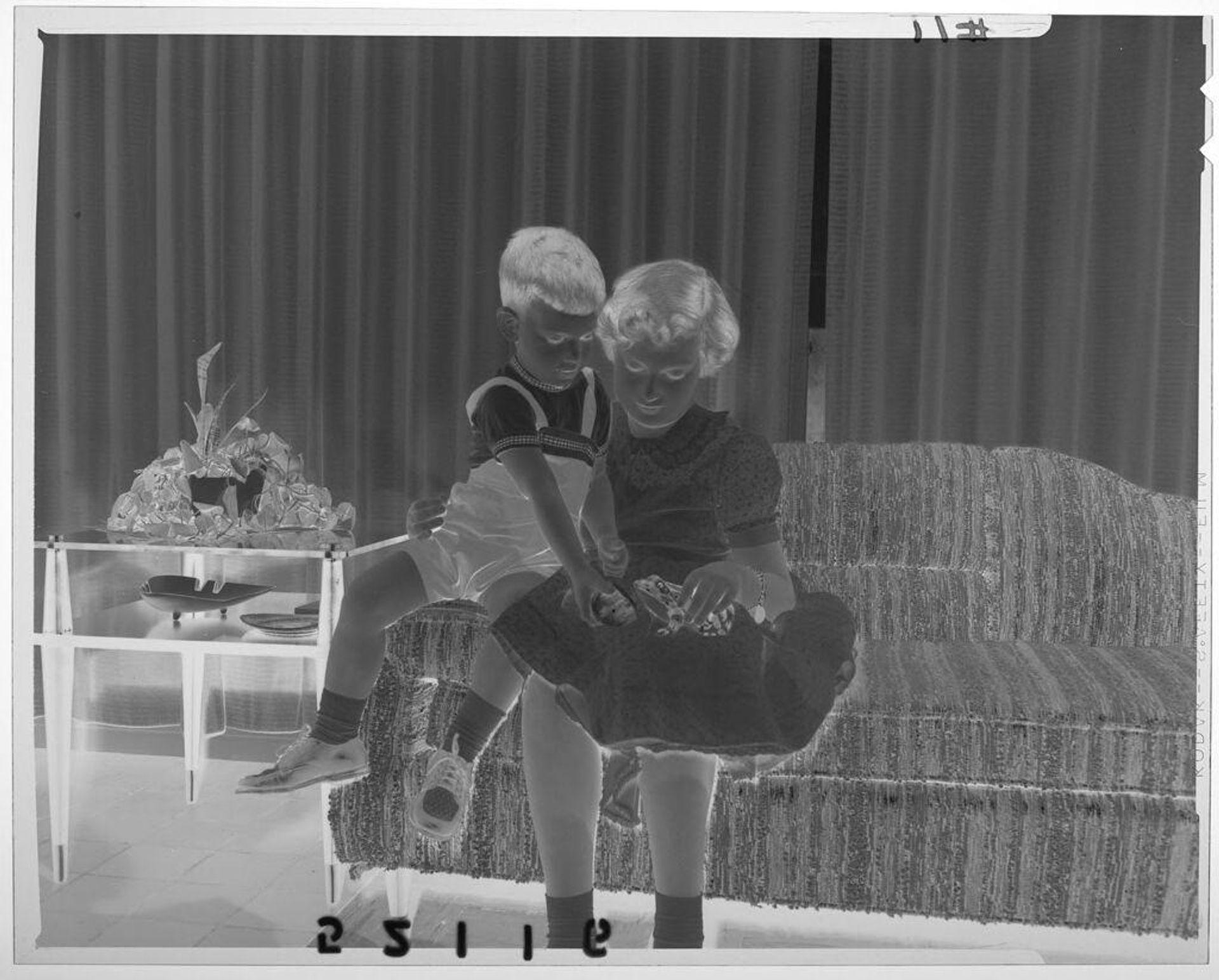 Untitled (girl and young boy looking at toy frog while sitting on living room couch) by Martin Schweig