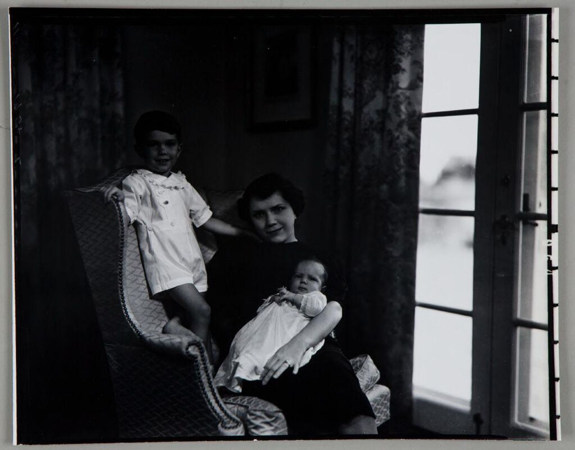 Untitled (mother seated with baby on lap in chair, little boy standing on chair to her side) by Paul Gittings