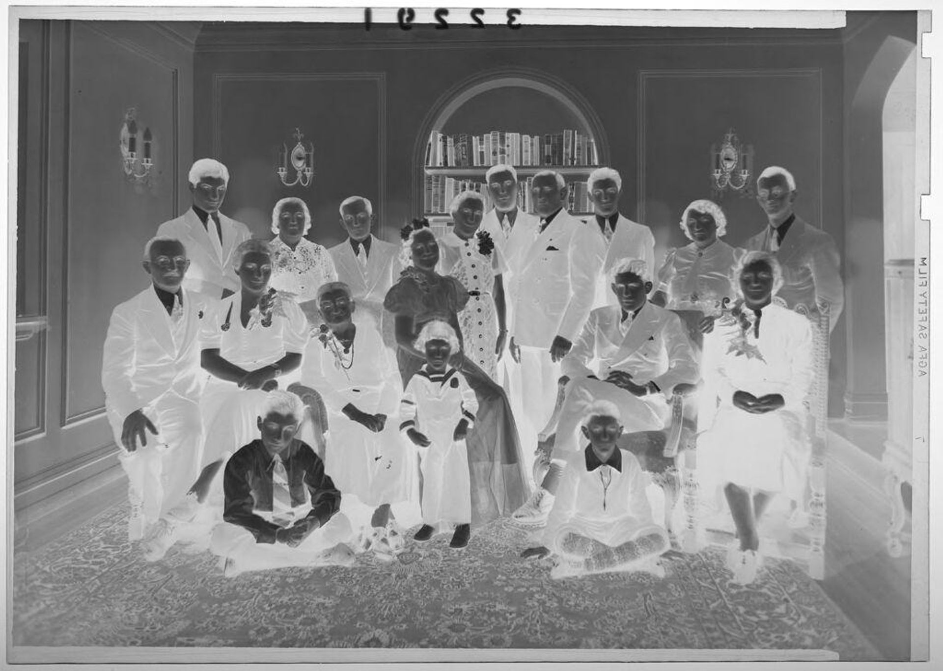 Untitled (large family of eighteen people posing in small room with bookshelf) by Martin Schweig
