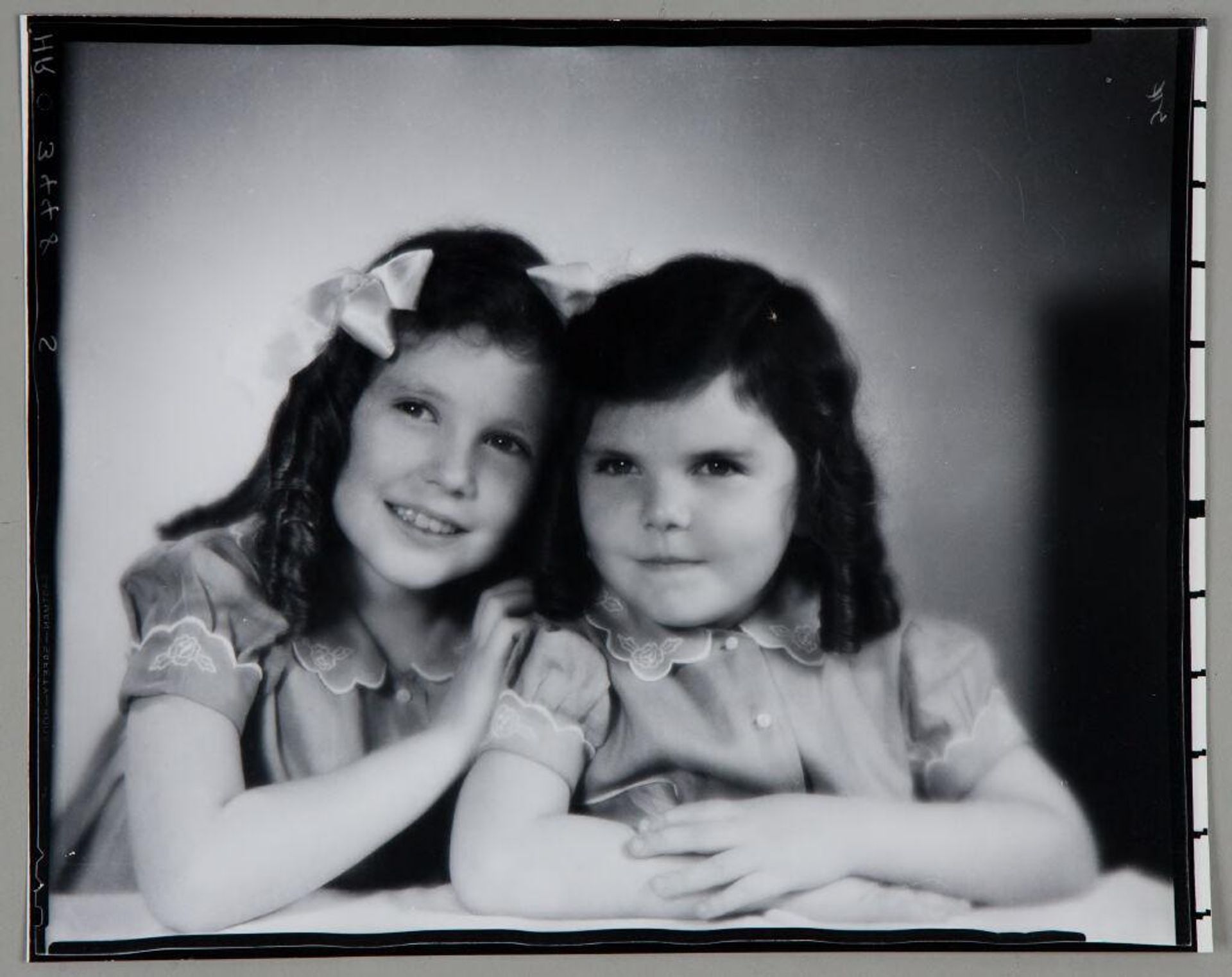 Untitled (two girls in matching dresses and brown ringlets seated together and leaning on table in front of them) by Paul Gittings