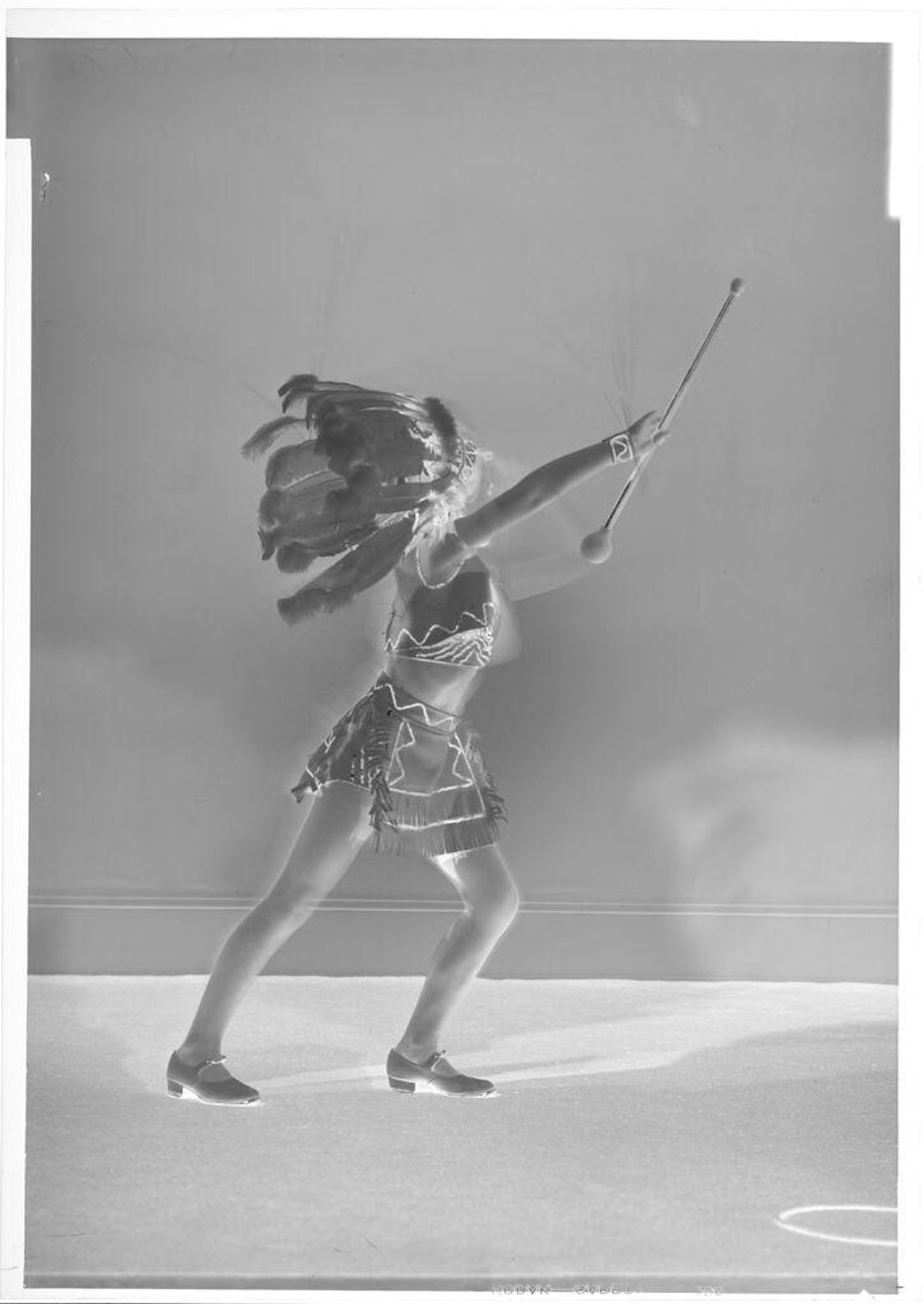 Untitled (girl in headdress and uniform with baton, reaching up) by John Deusing