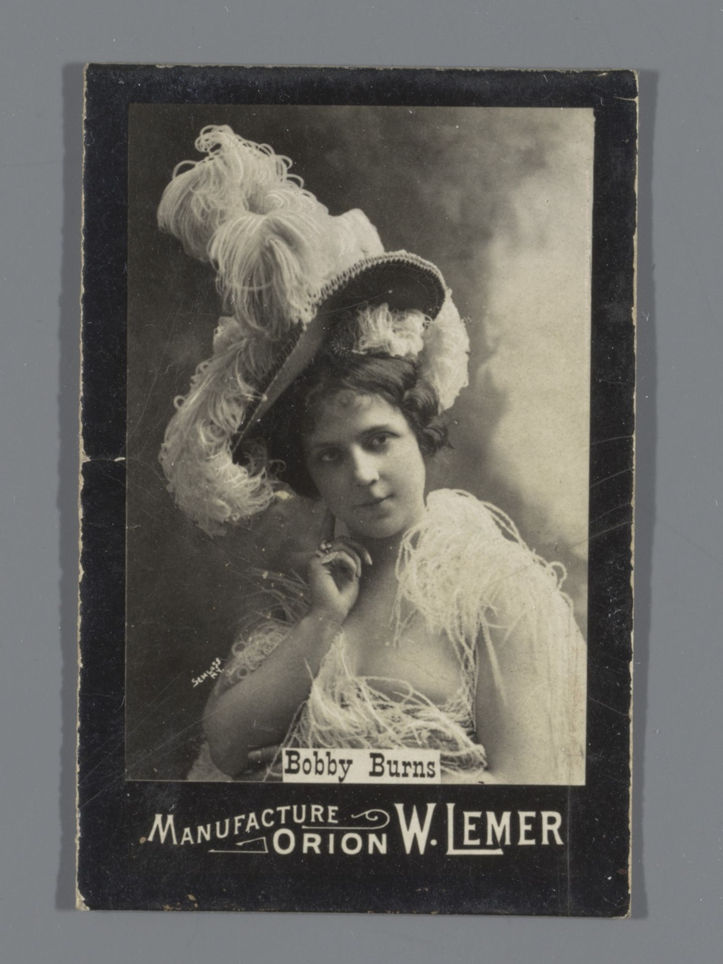 Portret van Bobby Burns met struisvogelveren, reclame voor Orion W. Lemer by J. Schluss