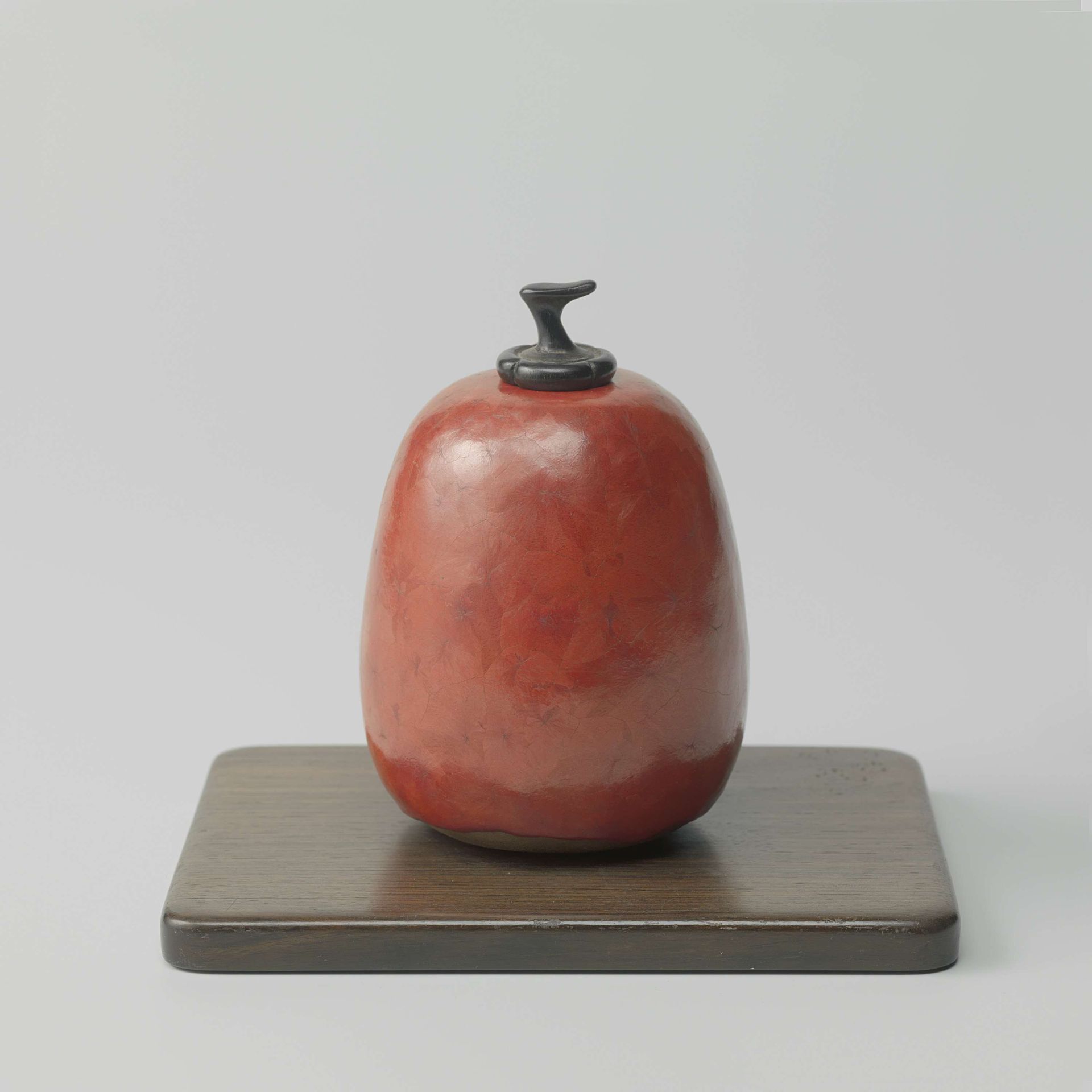 Pot, peervormig, met rode glazuur en een houten stopje, staande op een houten plankje by Henry Simmen