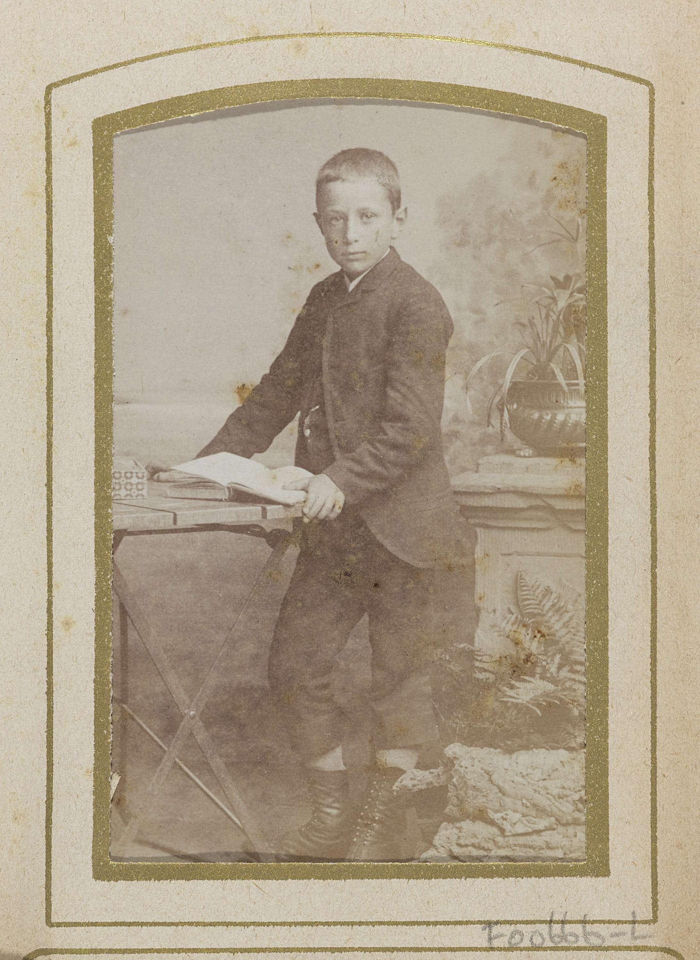 Portret van een jongen met een boek op een tafel, met op de achtergrond een sokkel by Jan Goedeljee