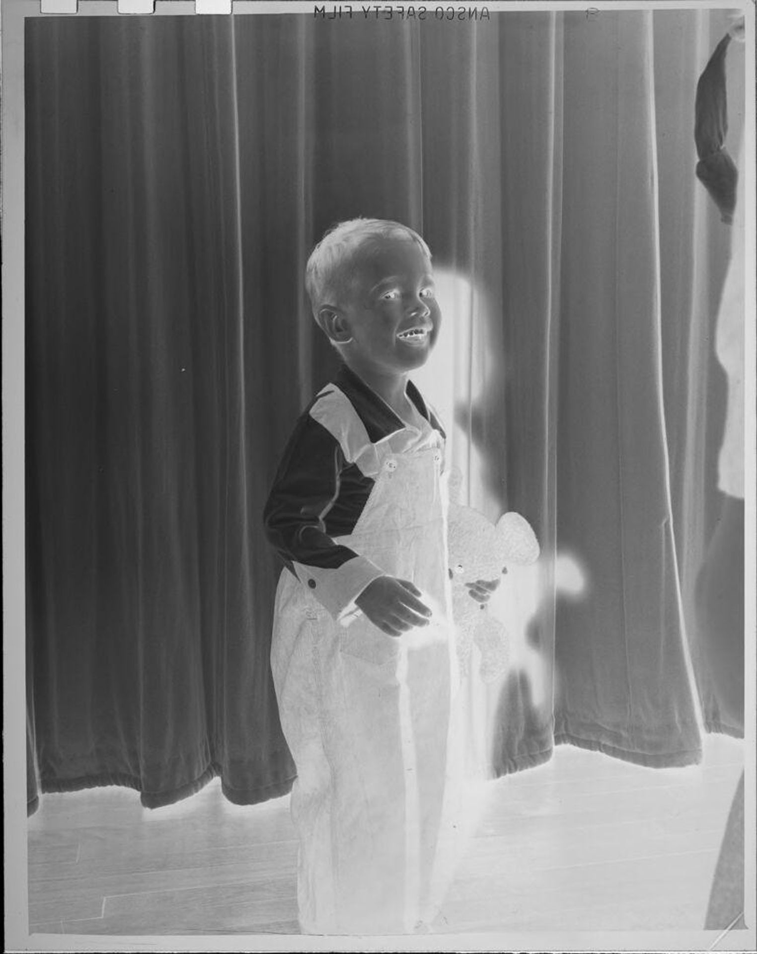 Untitled (boy wearing overalls holding stuffed bear) by Lucian and Mary Brown