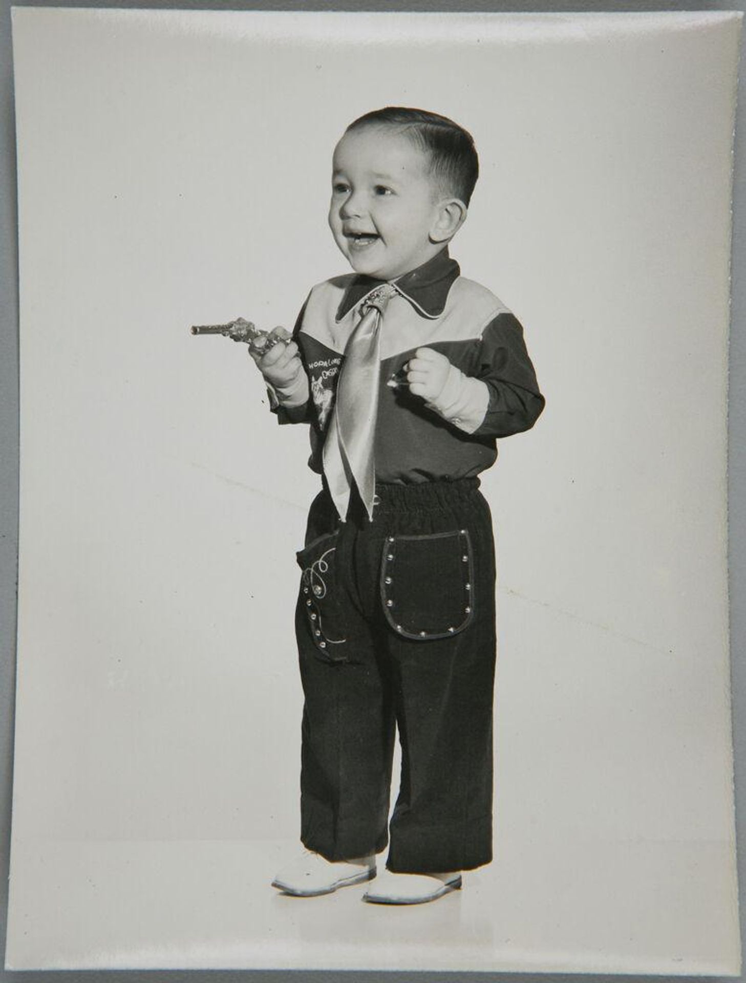 Untitled (little boy in cowboy outfit, holding gun, smiling) by John Deusing