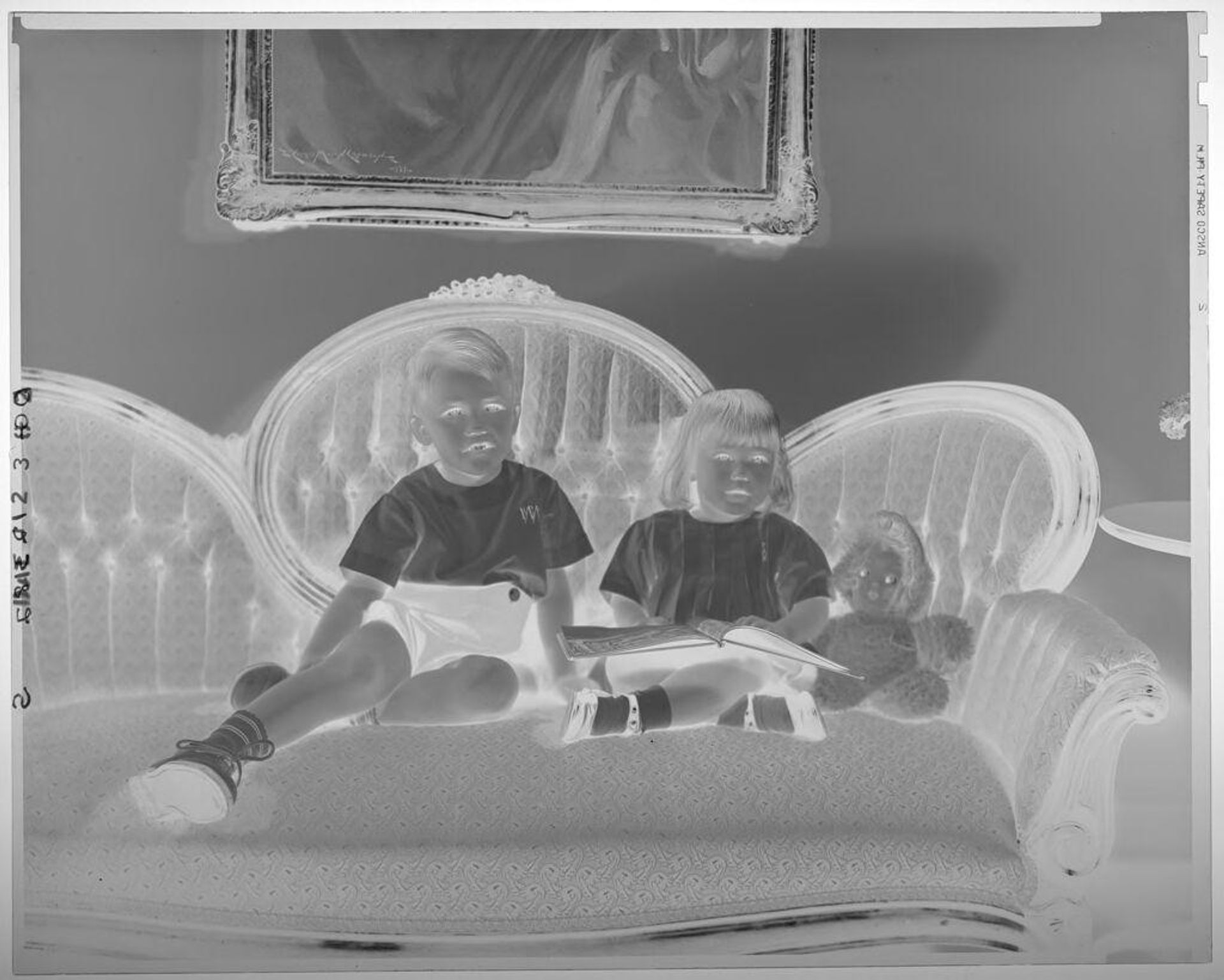 Untitled (brother and sister seated on sofa under painting, legs crossed; girl has open book on lap) by Paul Gittings