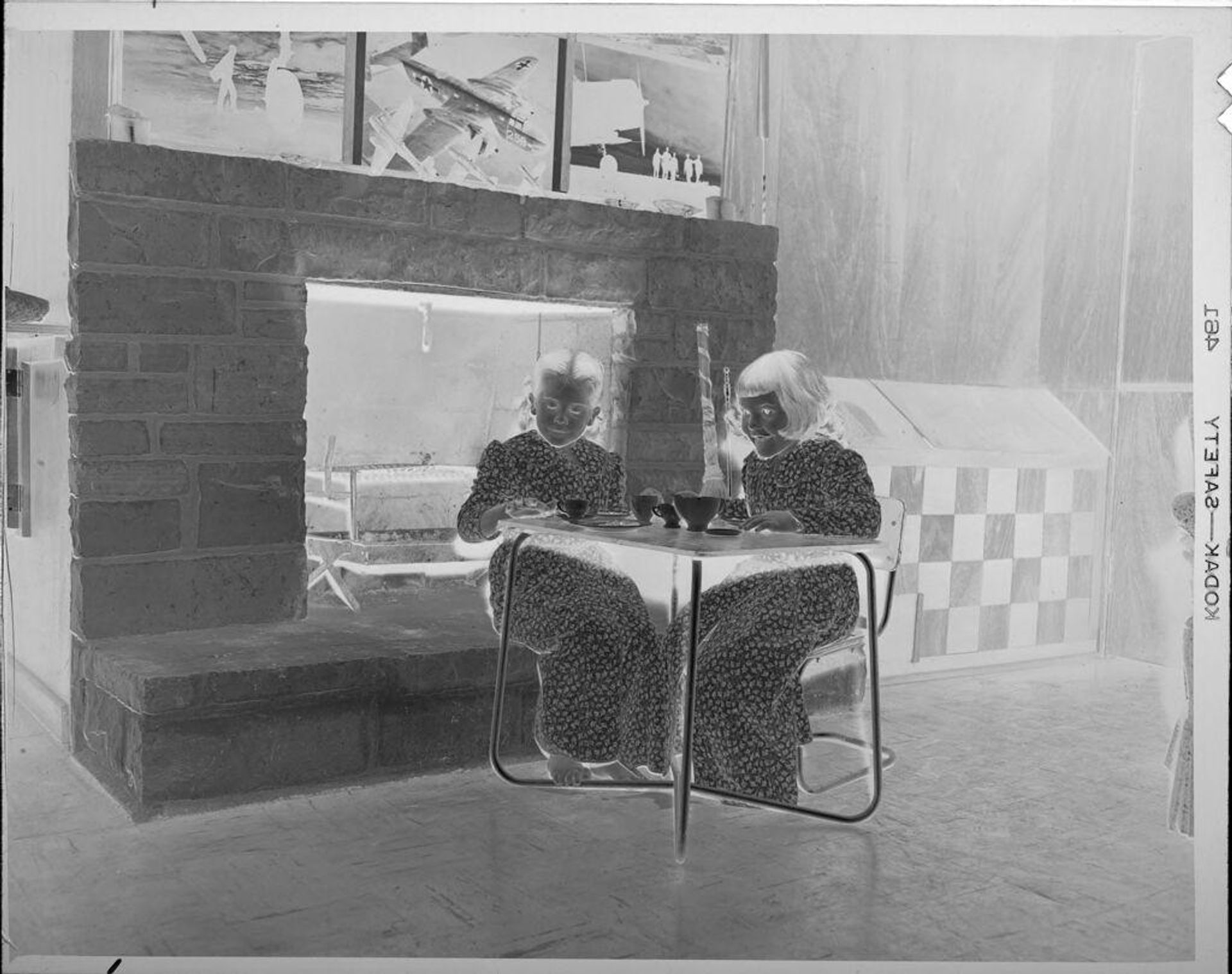 Untitled (two girls sitting at little table in front of fireplace) by Lucian and Mary Brown