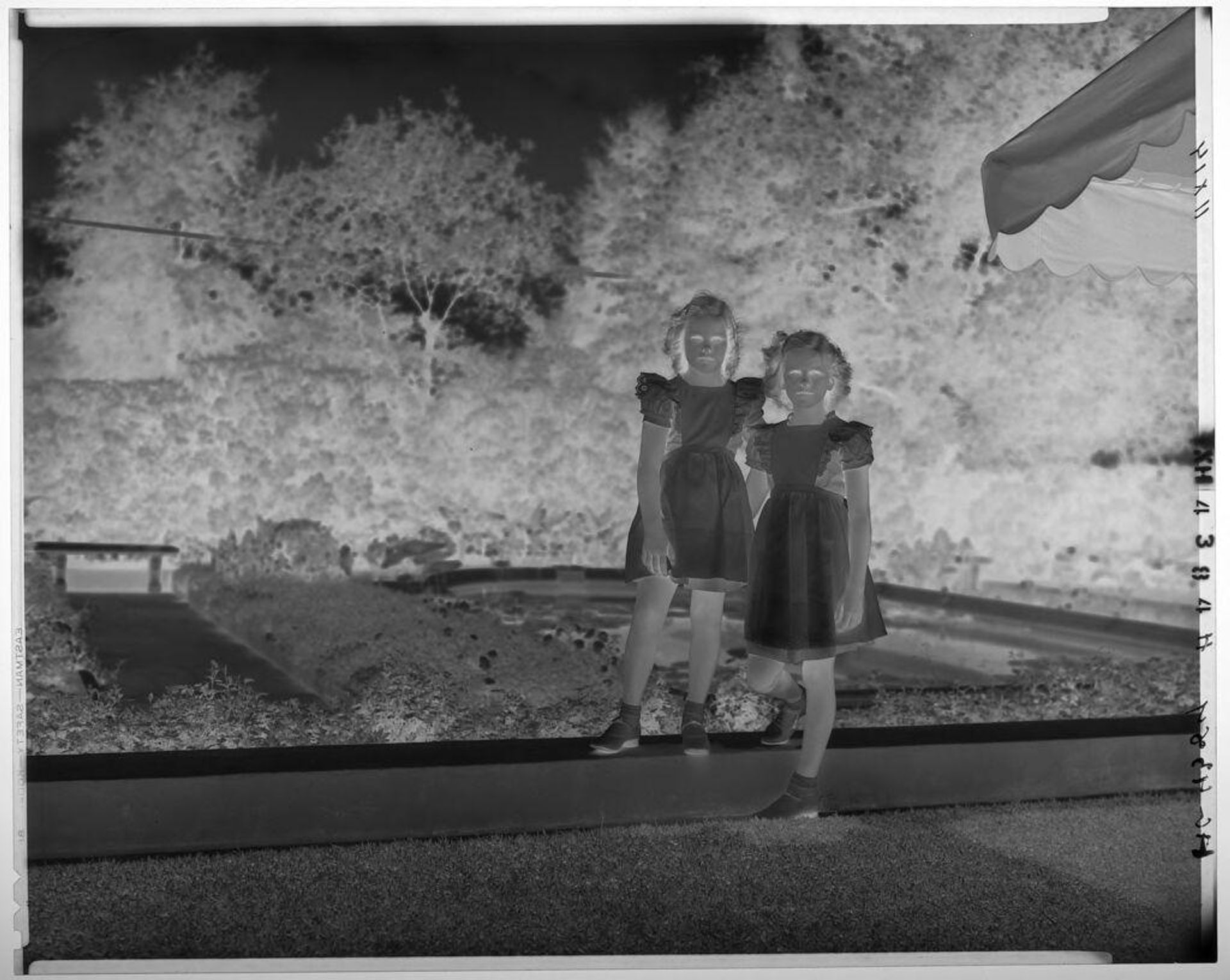 Untitled (two girls in matching dresses standing on ledge in yard) by Paul Gittings