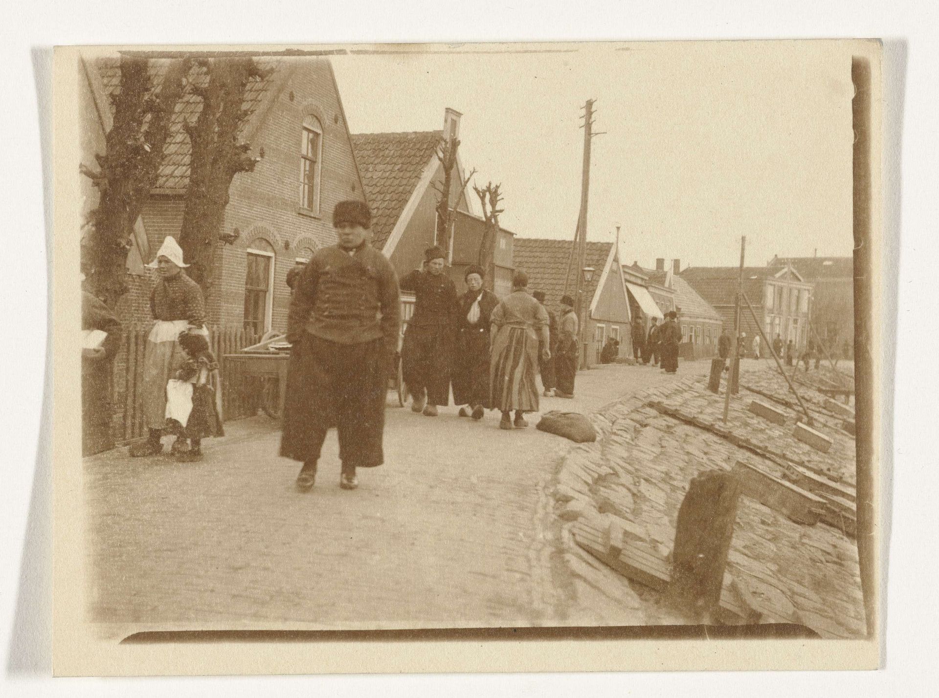Gezicht op een dijk in Volendam met mensen in klederdracht by G. Hidderley